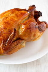 Homemade tasty rotisserie chicken on a white plate on a white wooden background, low angle view. Close-up.