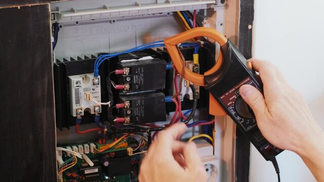 Electricians hands testing current  electric in control panel. Electrician engineer work  tester measuring  voltage and current of power electric line in electical cabinet control.