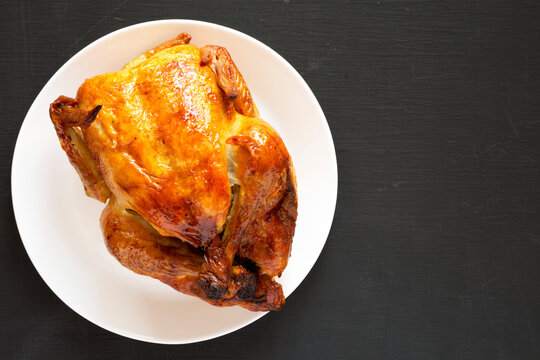 Homemade traditional rotisserie chicken on a white plate on a black background, top view. Flat lay, overhead, from above. Space for text.