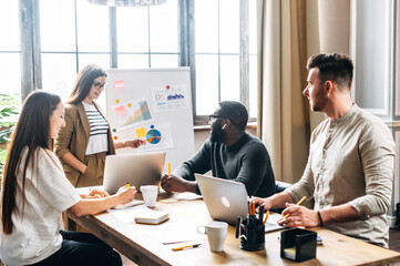 A young confident woman conducts a presentation to employees in the office, a woman in glasses points on flip chart and explains something to multiracial team of coworkers