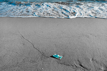 A blue face mask is left abandoned on the beach. It must be disposed in a proper hazardous waste bin, preventing germs spread. Corona Virus Covid19. Objects and medical supply. .