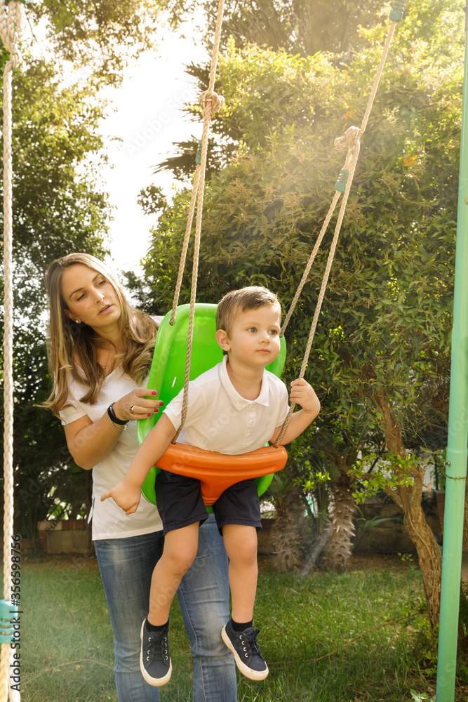 Wall mural mamma bionda spinge il figlio nell'altalena del giardino di casa