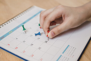 young woman's hand hold red push pin to marked on calendar