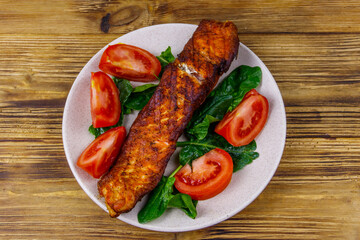 Grilled salmon fillet with spinach and tomatoes on wooden table. Top view