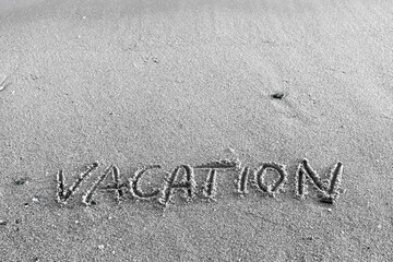 Vacation word handwritten on sandy beach natural outdoors background.