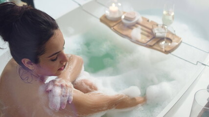 Smiling woman washing hands with foam. Sexy girl relaxing in bath with candles