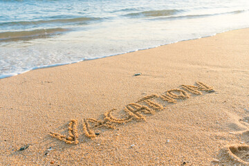 Vacation word handwritten on sandy beach natural outdoors background.