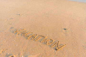 Vacation word handwritten on sandy beach natural outdoors background.
