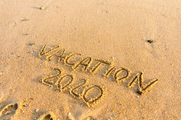 2020 Vacation handwritten on sandy beach natural outdoors background.