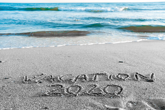2020 Vacation handwritten on sandy beach natural outdoors background.