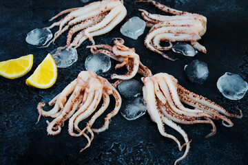 Close up raw fresh squid tentacles on a black concrete background, top view, text space