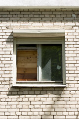 An old broken clogged window in a white brick apartment building.