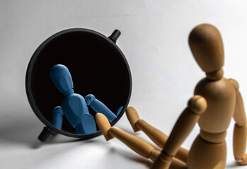 A toy wooden figure sits in front of the mirror. Reflection of a wooden figure in the mirror. Idea for the topic of psychology