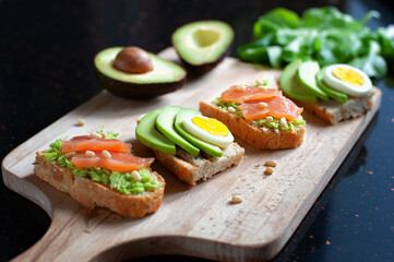 sandwiches with avocado, sliced egg, red fish and pine nuts on a wooden cutting board