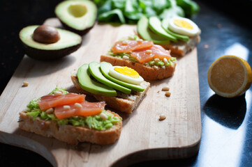 lemon and sandwiches with avocado, sliced egg, red fish and pine nuts on a wooden cutting board on the dark stone countertop