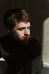 Obraz premium A young bearded man sits thoughtfully on the sofa.