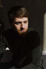 A young bearded man sits thoughtfully on the sofa.