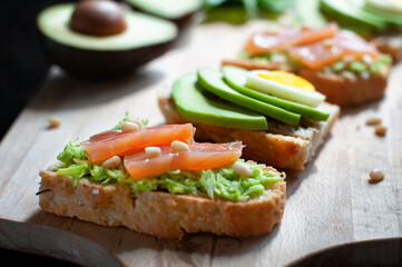 sandwiches with avocado, sliced egg, red fish and pine nuts on a wooden cutting board