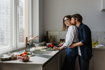 Young man and woman hugging and preparing salad together in the kitchen.