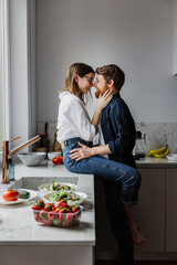 Beautiful young woman and man hugging and kissing in the kitchen.