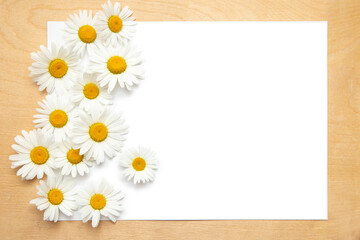 White paper card on rustic wooden background with chamomile. Flowers. Workspace. Blank for greetings