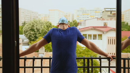 Revealing shot of man relaxing on balcony during covid-19 outbreak. Man in isolation.