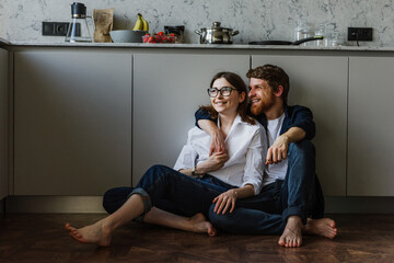 Naklejka premium Beautiful woman and man hugging and kissing while sitting on the floor in the kitchen.