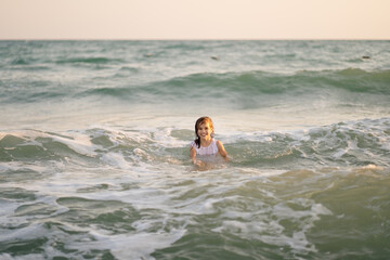 Fototapeta na wymiar teenager girl in dress swims in sea with high waves. entertainment in vacation. 