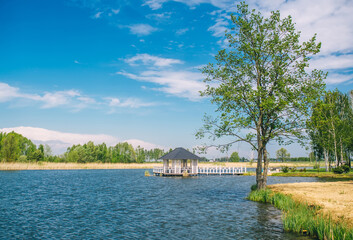 Gazebo with a bridge in the middle of a lake in the park in sunny warm day.