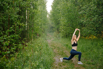 Attractive woman in sports clothes doing sports exercises on the road, loves gymnastics, stretching her legs. An active young girl is engaged in sports, leads a healthy lifestyle in the Park outdoors.