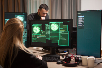 Back view of female hacker typing virus on computer. Male hacker in the background.