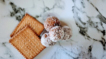 Chocolate and biscuits balls with coconut flacks with two whole biscuits sweet snack on marble background