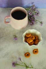 Ceramic coffee cup, bagels and lilac flowers on the table. Healthy breakfast in the morning