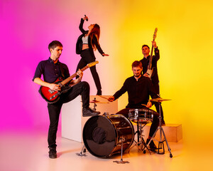 Fototapeta premium Young and joyful caucasian musicians performing on gradient studio background in neon light. Concept of music, hobby, festival. Colorful portrait of modern artist. Inspiring. Art, cover band.