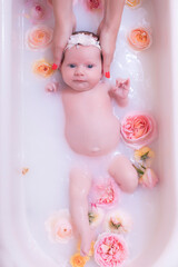 Happy kid girl takes a milk bath with petals. Bouquets of pastel rose flowers. Infant bathing. Hygiene and care for young children.