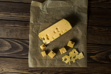 Maasdamer cheese. diced cheese in wrapping paper on an old black wooden table.
