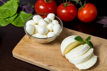  a large ball of mozzarella cheese sliced ​​on a wooden plate with basil leaves, tomatoes and hot pepper.