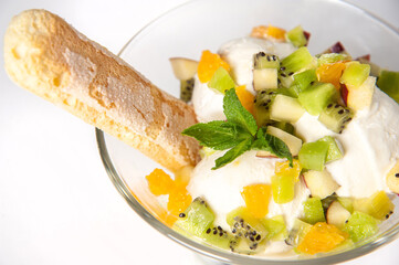 Balls of creamy cold ice cream with slices of fresh fruit: kiwi, mango, peach, grape. In the bowl. With biscuit sugar stick, garnished with a sprig of mint. Close-up.