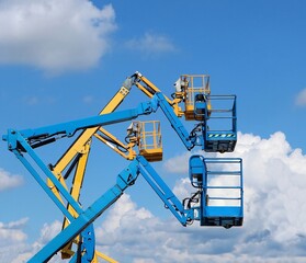 Four aerial work platforms against blue sky with fluffy clouds