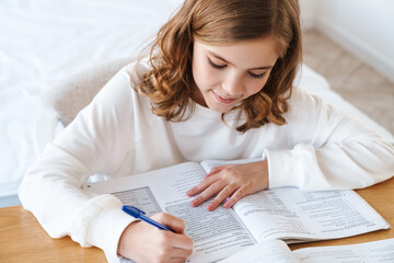 Photo of focused girl writing in exercise book while doing homework
