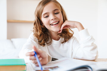 Photo of happy girl writing in exercise book while doing homework