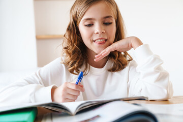 Photo of happy girl writing in exercise book while doing homework