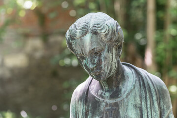 Nahaufnahme einer weiblichen Bronzestatue Frau mit kurzen Haaren mit Kreuz und Strickjacke in einem Park, Deutschland