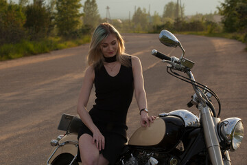 A woman in a black dress  on a motorcycle against the background of trees.