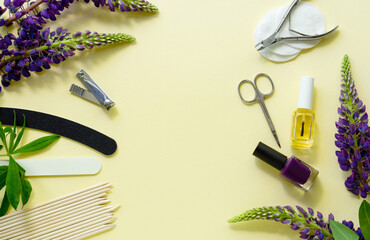 Manicure and pedicure items with lupin flowers on a light yellow background. Space for text