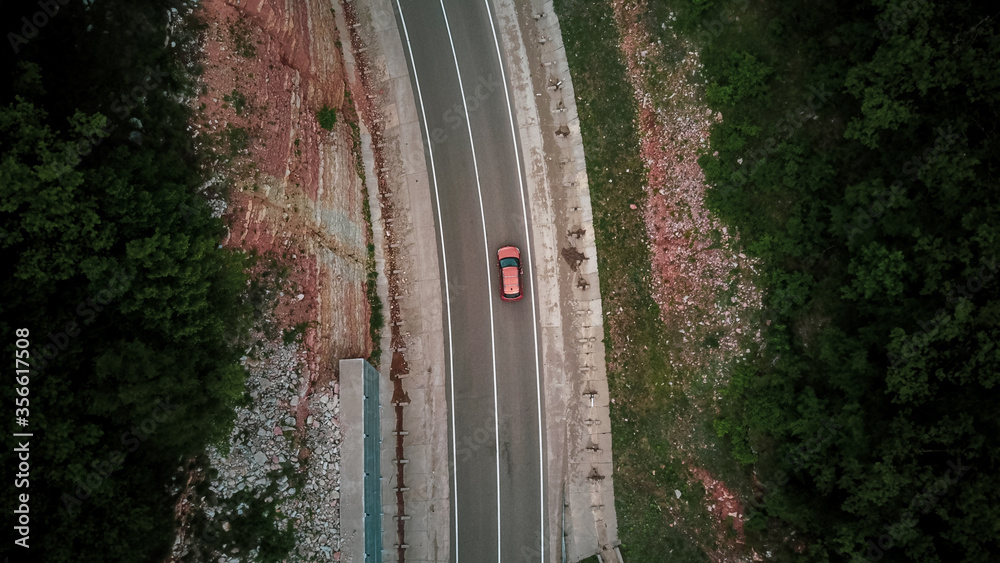 Wall mural drone point of view: aerial view flying over two lane countryside forest road with orange car moving