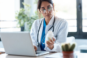 Concentrated female doctor writes the medical prescription in a laptop in the consultation.