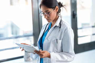 Beautiful female doctor using her digital tablet while standing in the consultation.