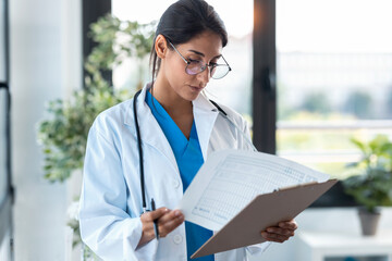 Beautiful female doctor reviewing medical documents while standing in the consultation.