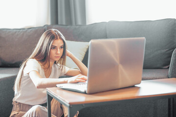 Young woman with modern laptop sitting on sofa at home